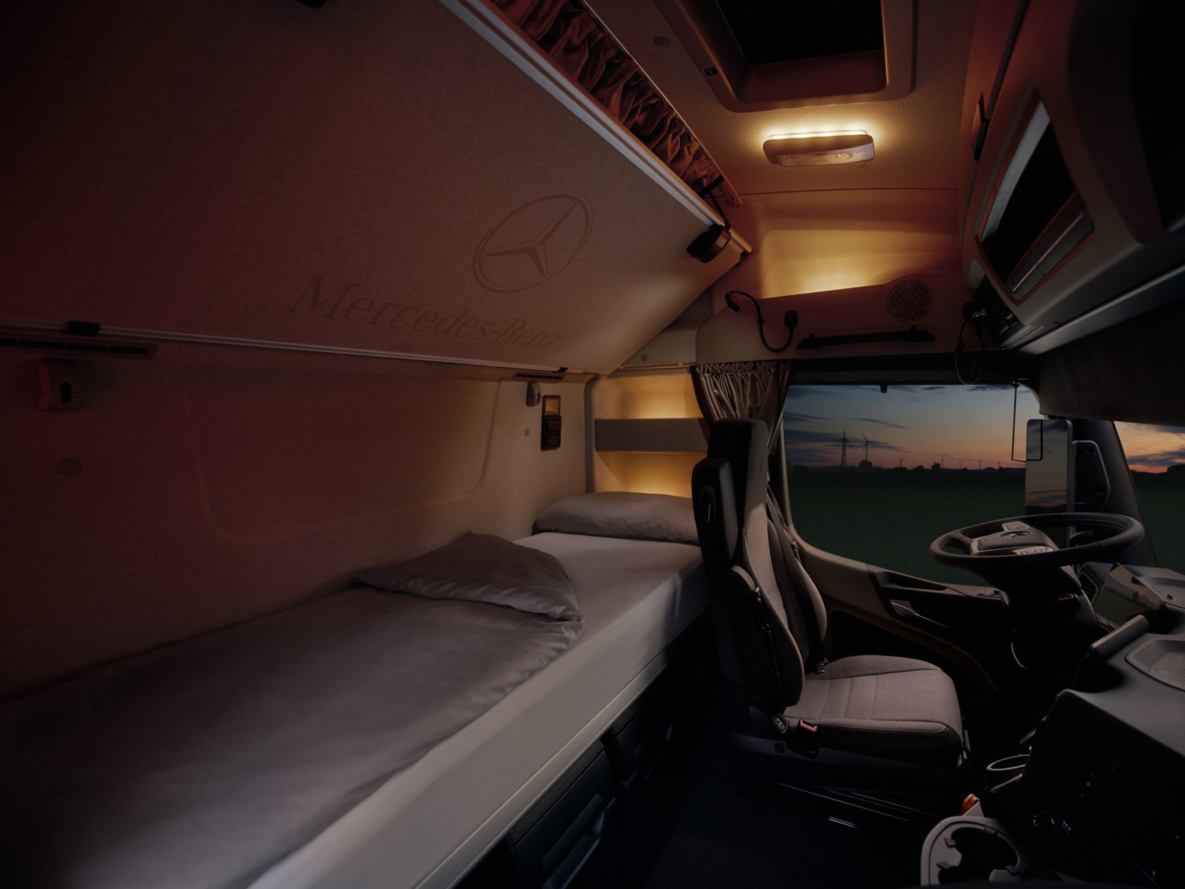 The image shows the interior of the cab of an eActros from Mercedes-Benz Trucks at dusk, with a view of the bed and driver’s seat. Wind turbines and a field at sunset can be seen through the windscreen, which creates a calm atmosphere.