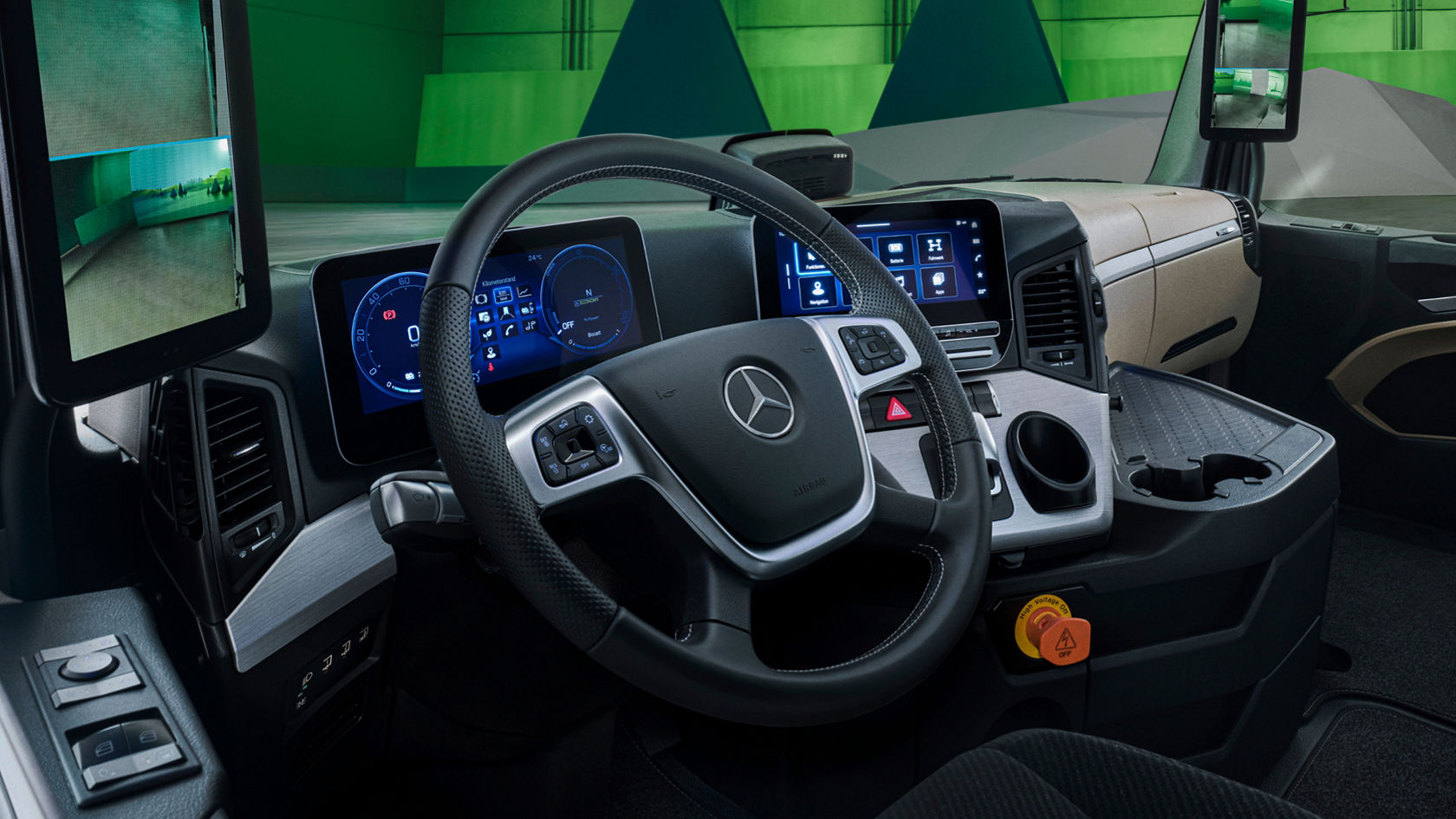The image shows the modern interior of the eActros from Mercedes-Benz Trucks with a digital cockpit and two large screens that replace the exterior mirrors. In the background is a green wall with geometric shapes that represents a stylised landscape.