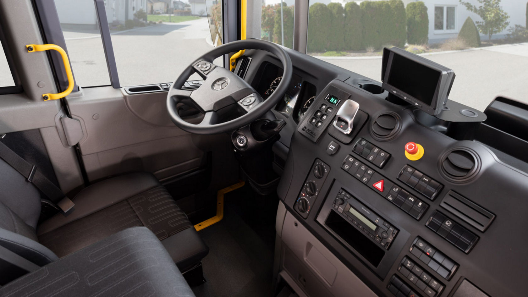 Interior view of the Econic with steering wheel, dashboard and driver’s seat. A residential street can be seen through the windscreen.