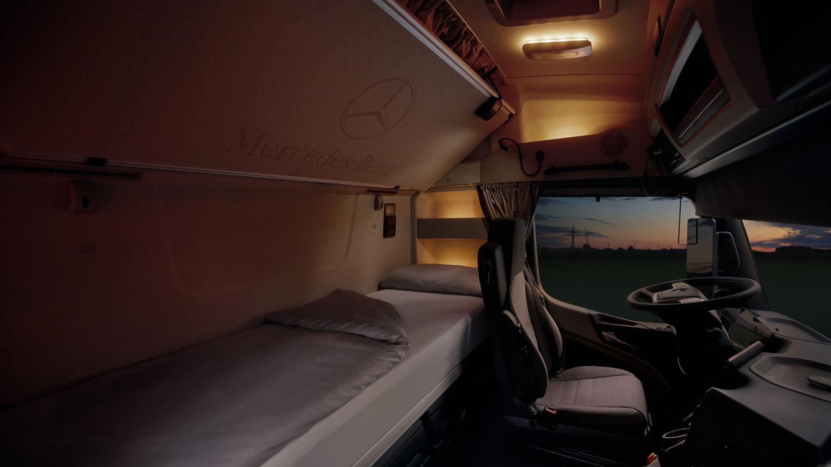 The image shows the interior of the cab of an eActros from Mercedes-Benz Trucks at dusk, with a view of the bed and driver’s seat. Wind turbines and a field at sunset can be seen through the windscreen, which creates a calm atmosphere.