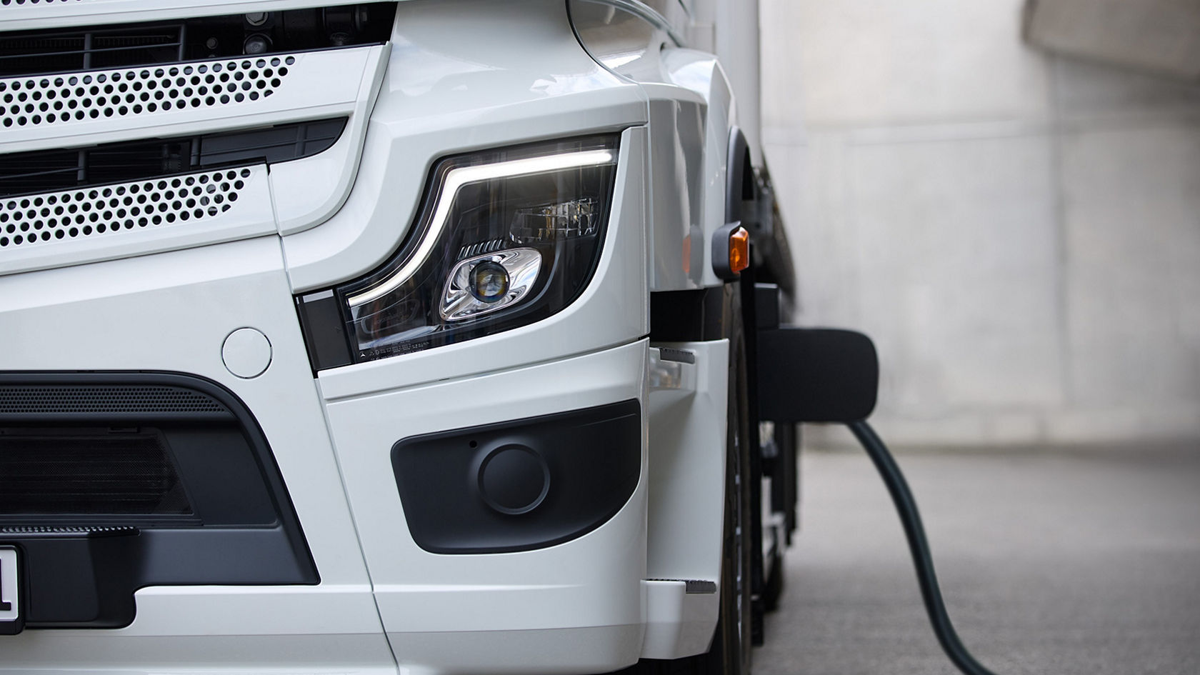 An eActros 600 from Mercedes-Benz Trucks is photographed from the right side, with the focus on the front area of the truck. The vehicle is white and a charging cable is connected to the side of the truck, indicating that the battery is charging.