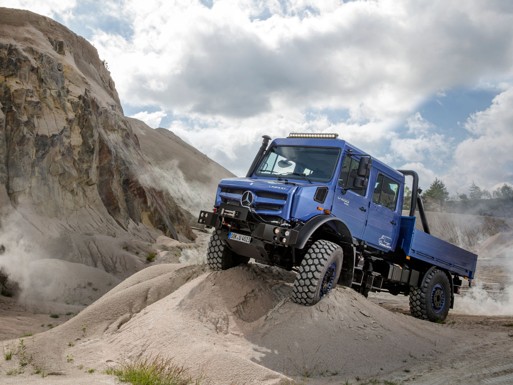 A blue Unimog climbing a steep sand dune.