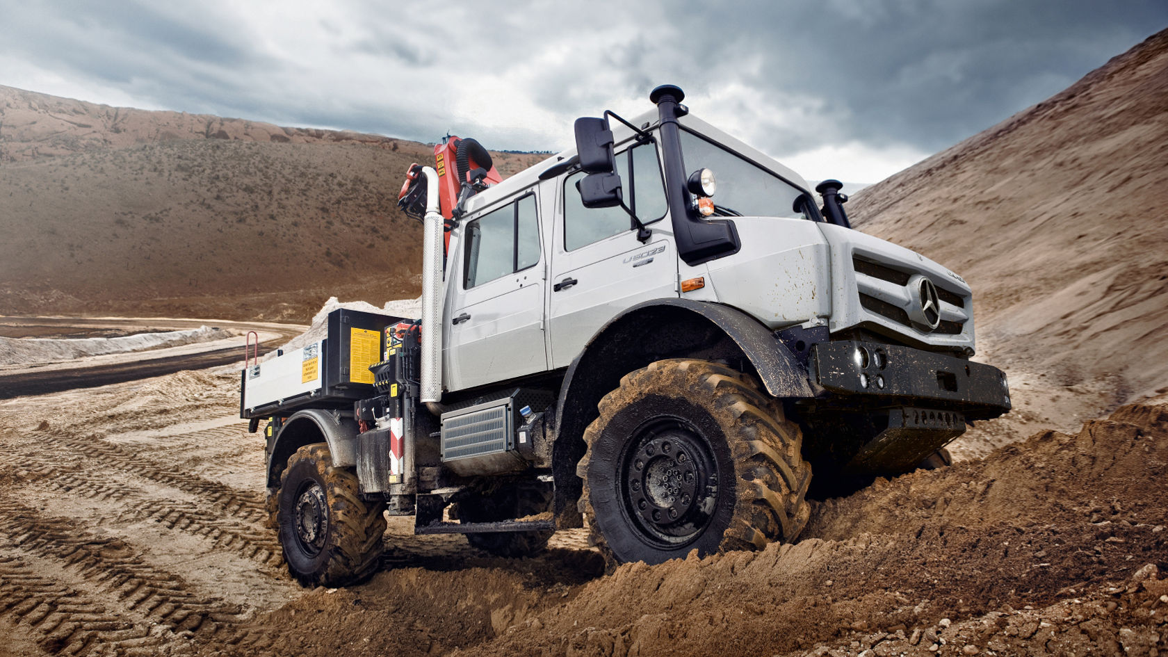 A white Unimog driving through sandy terrain.
