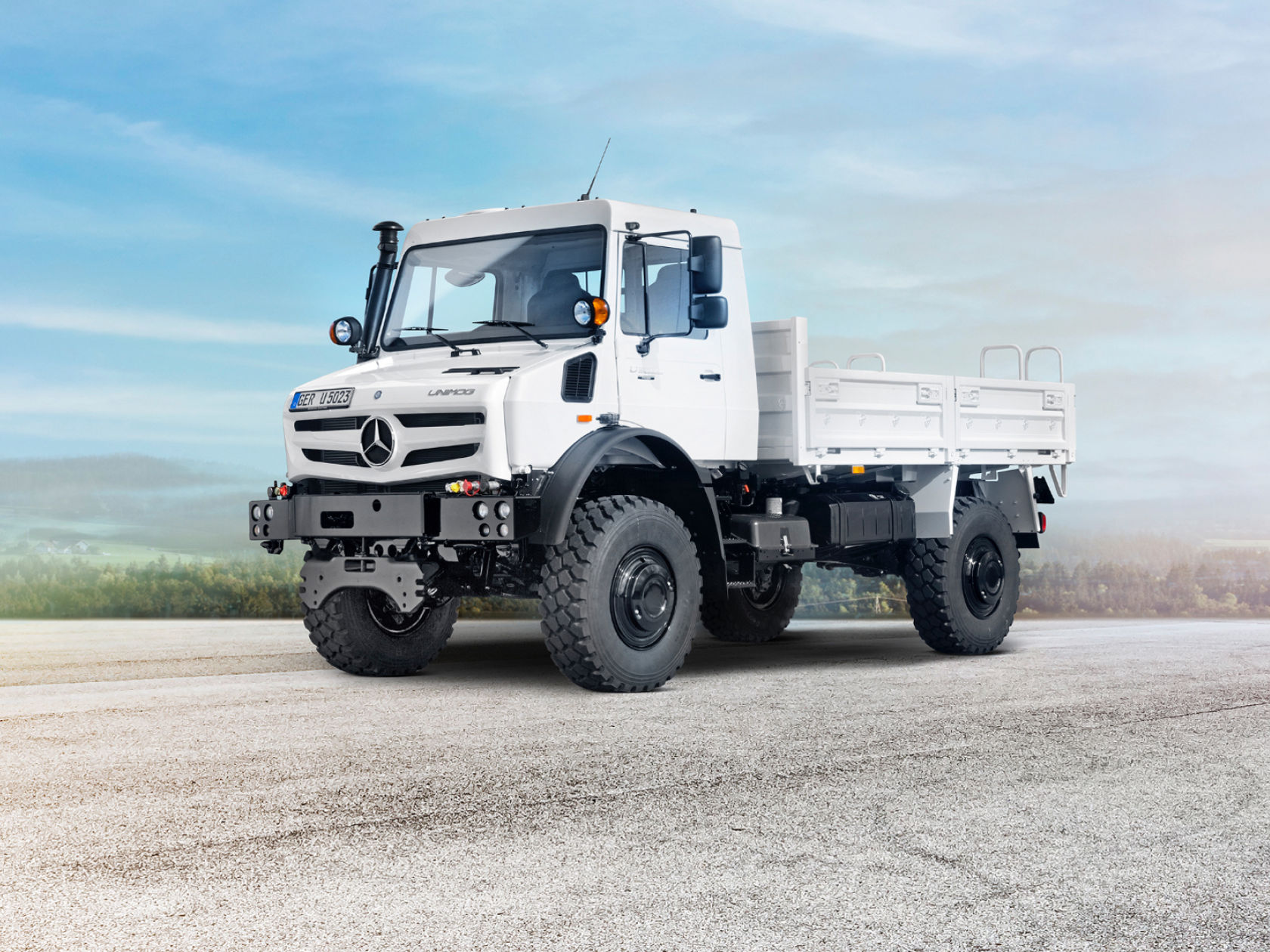 A white Unimog standing on a road in a rural setting.