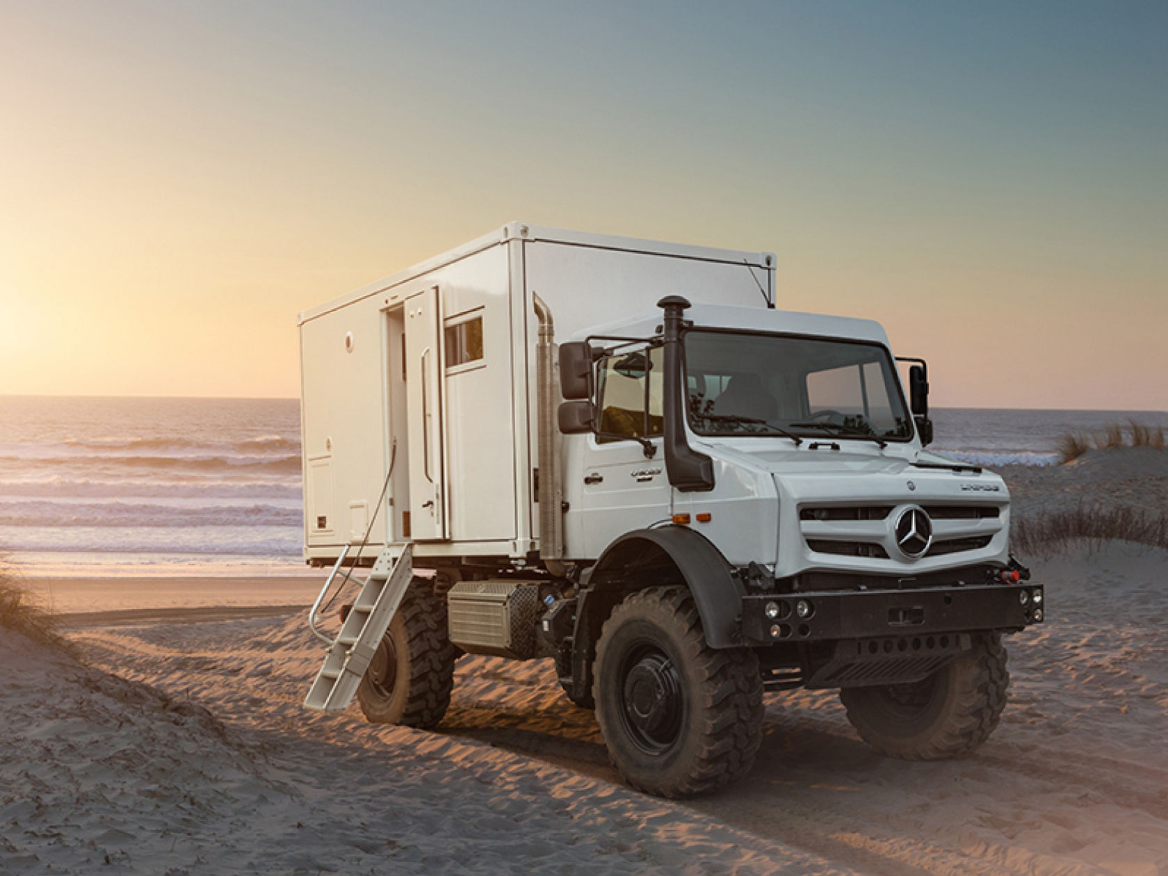 A white Unimog standing on the beach. 