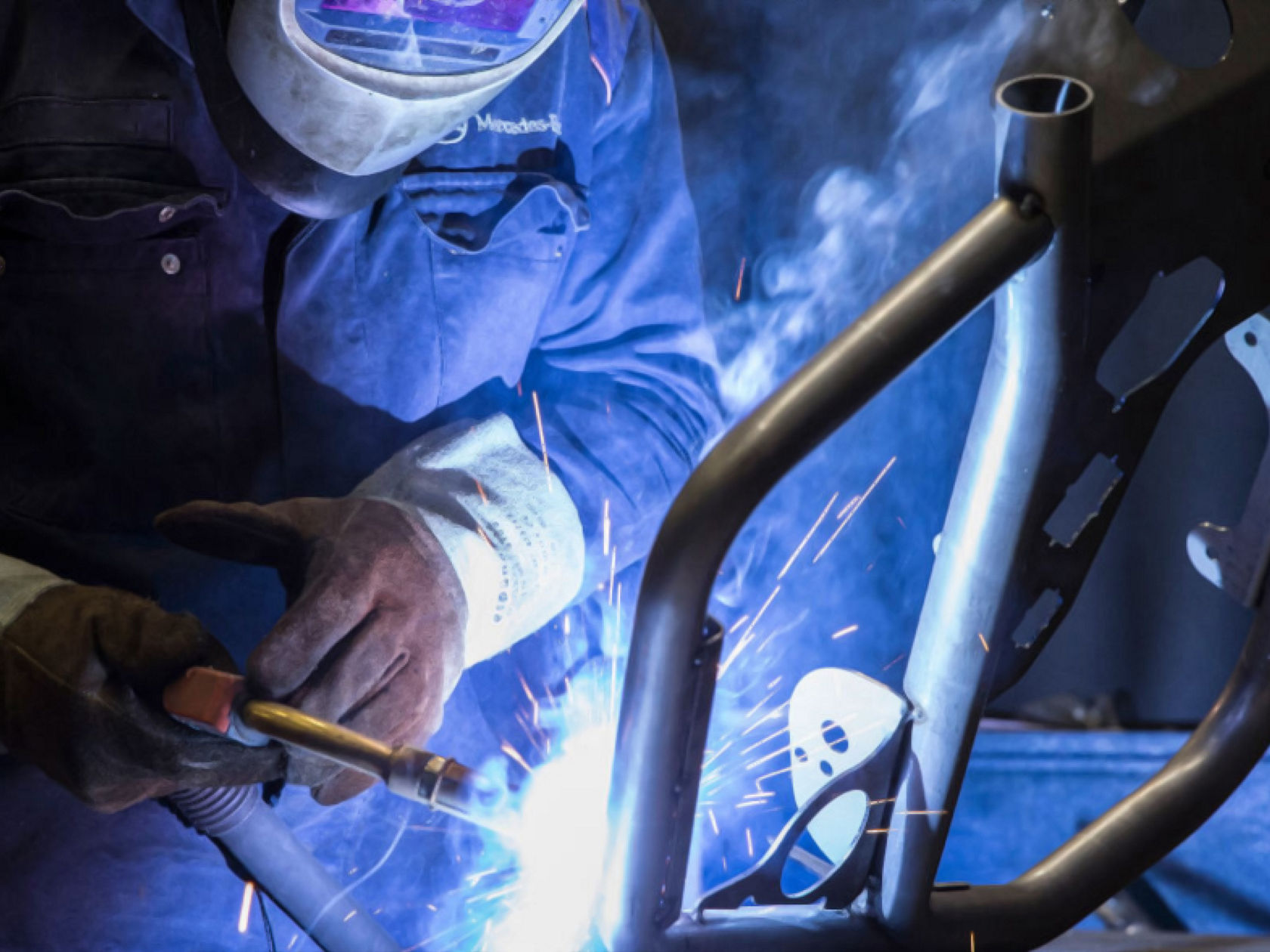 Welder wearing a safety helmet and gloves welding a metal part.