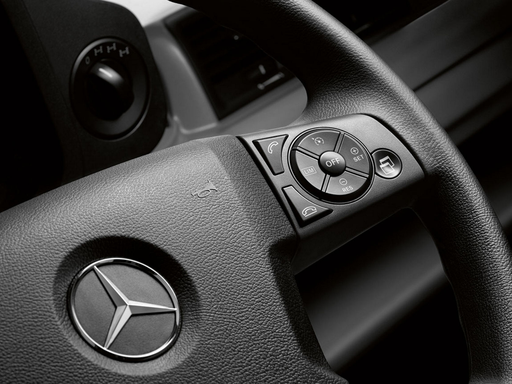 The interior of a vehicle cab with steering wheel, dashboard and driver’s seat. A cloudy sky can be seen through the windscreen.