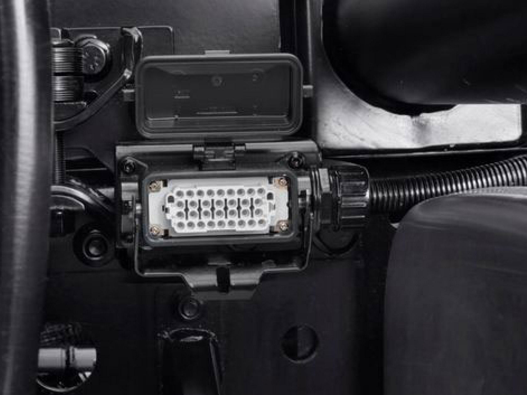 Close-up of an electrical connection. The connector is attached to a black metal frame and has a small, folded-up cover.