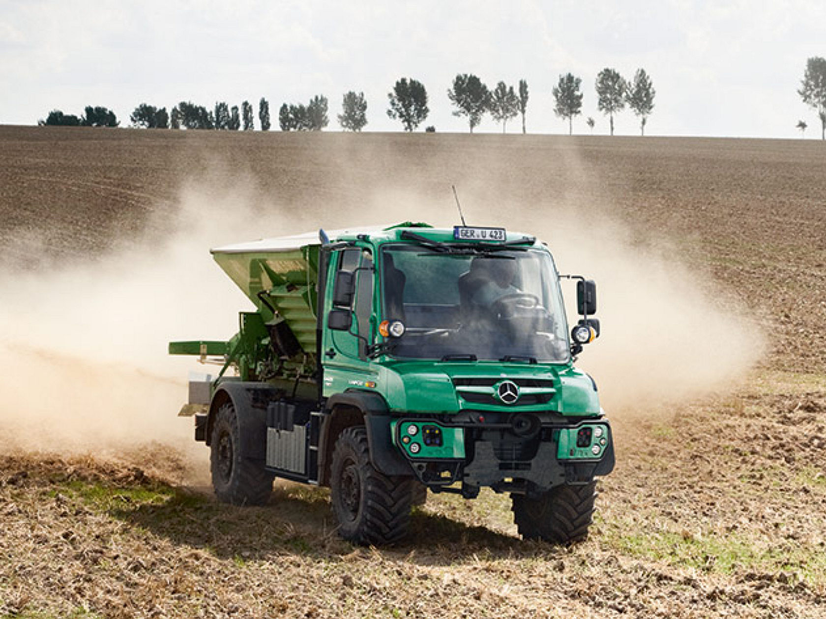 A green Unimog implement carrier in agricultural operation drives over a field.